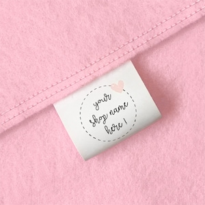 May include: A pink fabric label with a white circle and the text "your shop name here!" inside the circle. A pink heart is above the text.