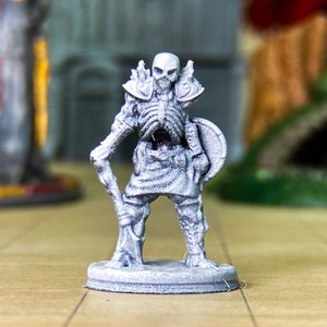 May include: A gray painted miniature skeleton warrior figure holding a staff and a shield. The figure is standing on a round base.