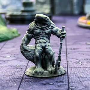 May include: A gray painted miniature figurine of a shark-like creature sitting on a rock with a spear in its hand.