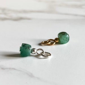 May include: Two green gemstone charms with silver and gold chain links. The charms are faceted and have a dark green color.