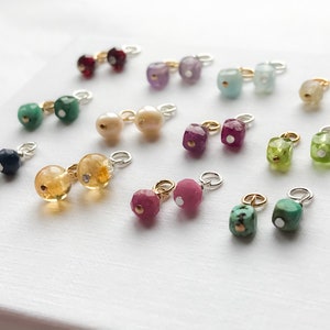 May include: Assortment of colorful gemstone charms with silver and gold accents. The charms are in various shapes and sizes, including square, round, and oval. The gemstones are set in silver or gold settings and have a polished finish.