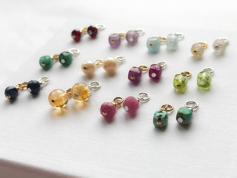 May include: Assortment of colorful gemstone charms with silver and gold accents. The charms are in various shapes and sizes, including square, round, and oval. The gemstones are set in silver or gold settings and have a polished finish.
