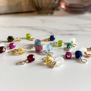 May include: Assortment of small, colorful gemstone charms with gold accents. Each charm features a different gemstone, including amethyst, aquamarine, citrine, garnet, peridot, ruby, sapphire, and topaz.
