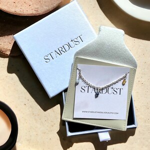 May include: A silver chain necklace with a variety of small, colorful stones hanging from it. The necklace is displayed in a white box with the word "STARDUST" printed on it.