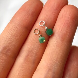 May include: Two green gemstone charms with gold jump rings. The charms are square shaped and have a shiny, polished finish.