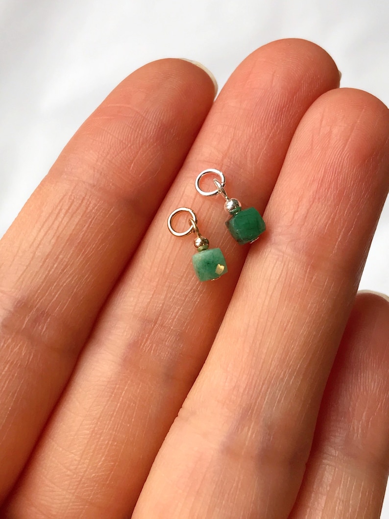 May include: Two green gemstone charms with gold jump rings. The charms are square shaped and have a shiny, polished finish.