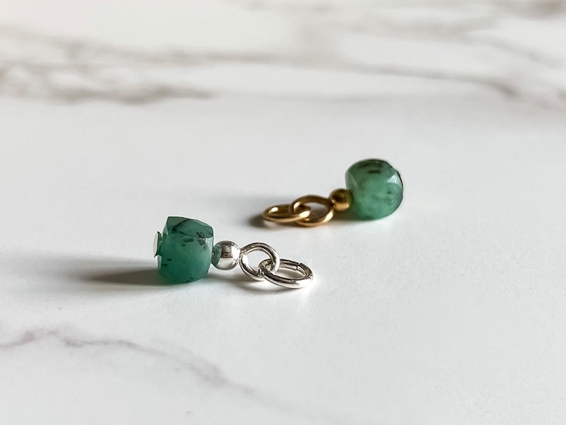 May include: Two green gemstone charms with silver and gold chain links. The charms are faceted and have a dark green color.