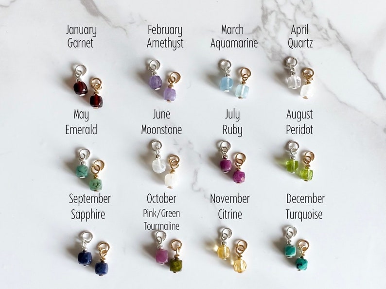 May include: Twelve small gemstone charms, each representing a different month of the year. The charms are arranged in four rows of three, with the month and gemstone name listed above each charm.