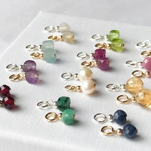 May include: A set of 12 gemstone charms with gold and silver jump rings. The charms feature various gemstones, including amethyst, aquamarine, emerald, ruby, sapphire, turquoise, and citrine.