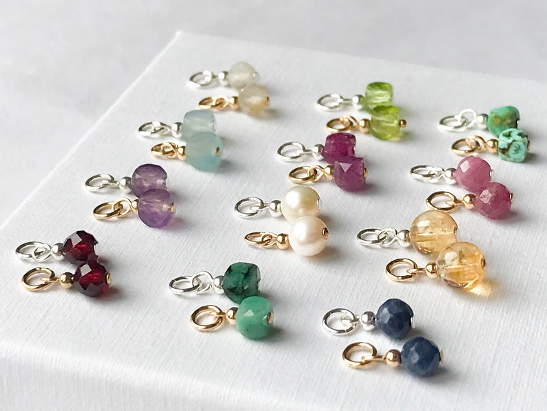 May include: A set of 12 gemstone charms with gold and silver jump rings. The charms feature various gemstones, including amethyst, aquamarine, emerald, ruby, sapphire, turquoise, and citrine.