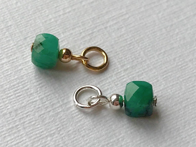 May include: Two green gemstone beads with gold and silver jump rings. The beads are faceted and have a square shape.