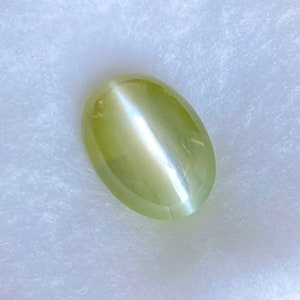 May include: A light green oval-shaped gemstone with a chatoyancy effect, also known as a cat's eye.