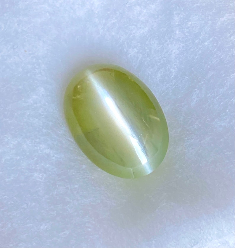 May include: A light green oval-shaped gemstone with a chatoyancy effect, also known as a cat's eye.
