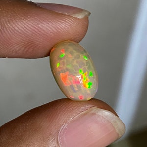 Pu&ograve; includere: Una pietra preziosa di opale ovale di colore grigio chiaro con bagliori verdi, rossi e arancioni.