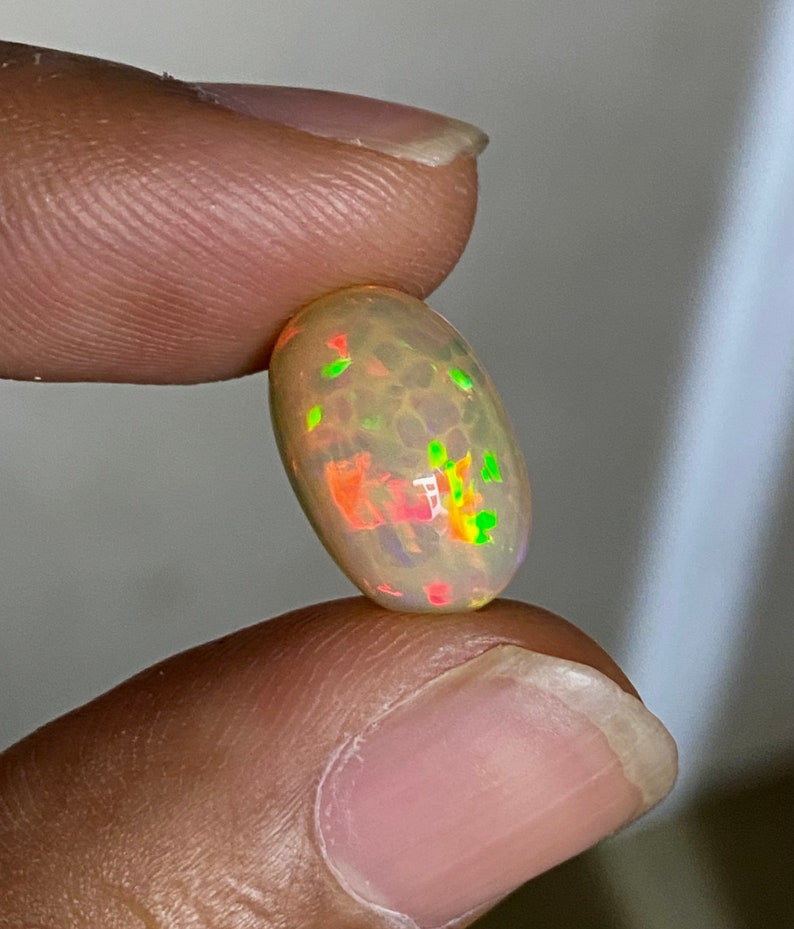 Pu&ograve; includere: Una pietra preziosa di opale ovale di colore grigio chiaro con bagliori verdi, rossi e arancioni.