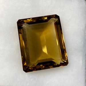 May include: A large, rectangular, faceted gemstone with a golden brown color. The gemstone is cut in an emerald shape.