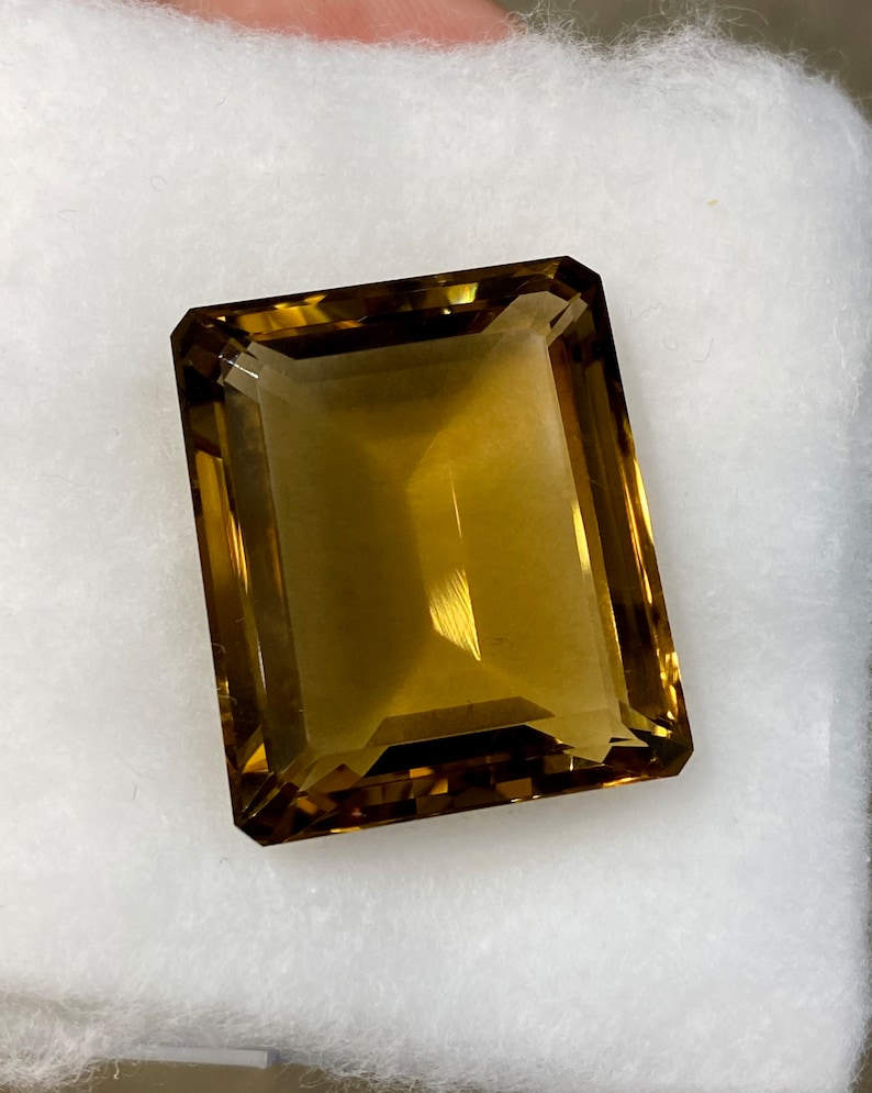 May include: A large, rectangular, faceted gemstone with a golden brown color. The gemstone is cut in an emerald shape.