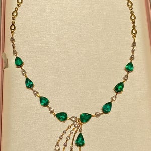 May include: A gold necklace featuring pear-shaped emeralds and small clear gemstones. The necklace has a delicate design with a central cluster of emeralds and a cascading arrangement of gems. The chain is gold.