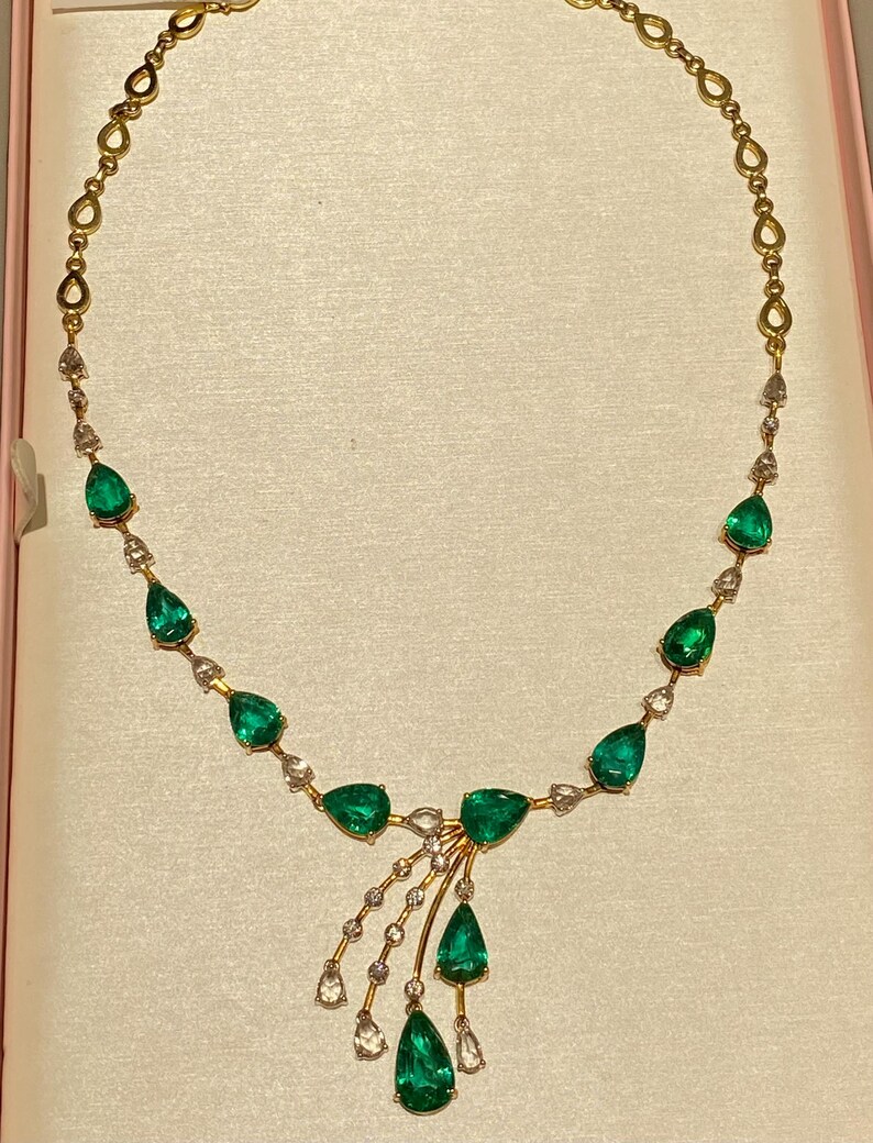 May include: A gold necklace featuring pear-shaped emeralds and small clear gemstones. The necklace has a delicate design with a central cluster of emeralds and a cascading arrangement of gems. The chain is gold.