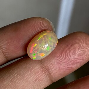 Pu&ograve; includere: Una pietra preziosa di opale ovale di colore marrone chiaro con bagliori di verde, arancione e rosso.