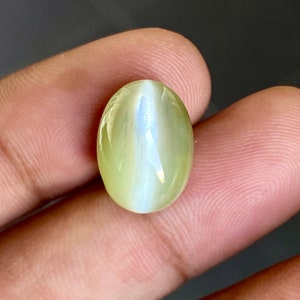 May include: A light green oval-shaped gemstone with a white iridescent sheen.