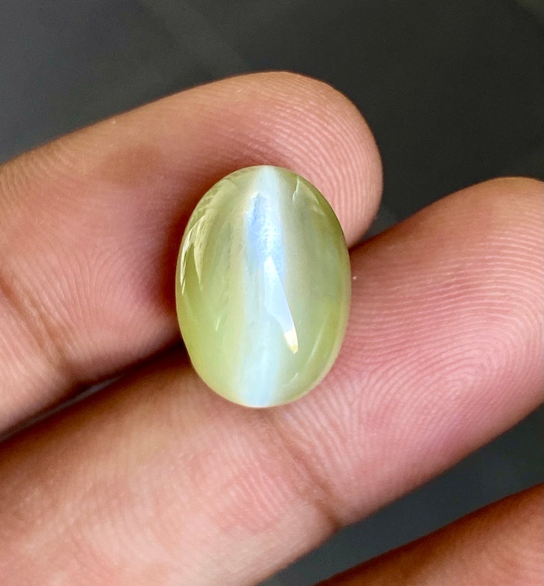 May include: A light green oval-shaped gemstone with a white iridescent sheen.