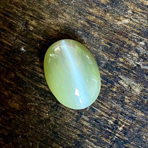 May include: A light green oval-shaped gemstone with a white iridescent sheen.