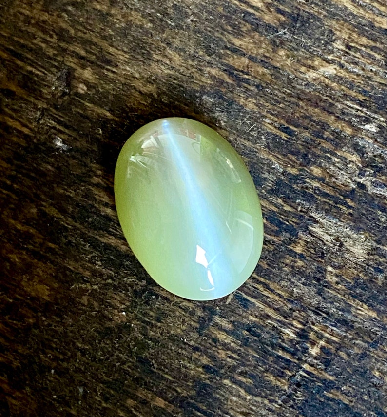May include: A light green oval-shaped gemstone with a white iridescent sheen.