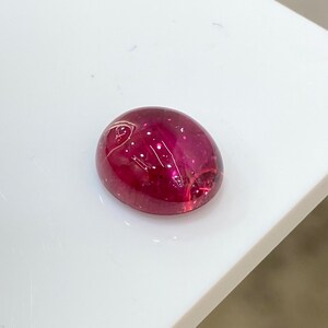 May include: A deep red oval cabochon gemstone with a smooth, polished surface.