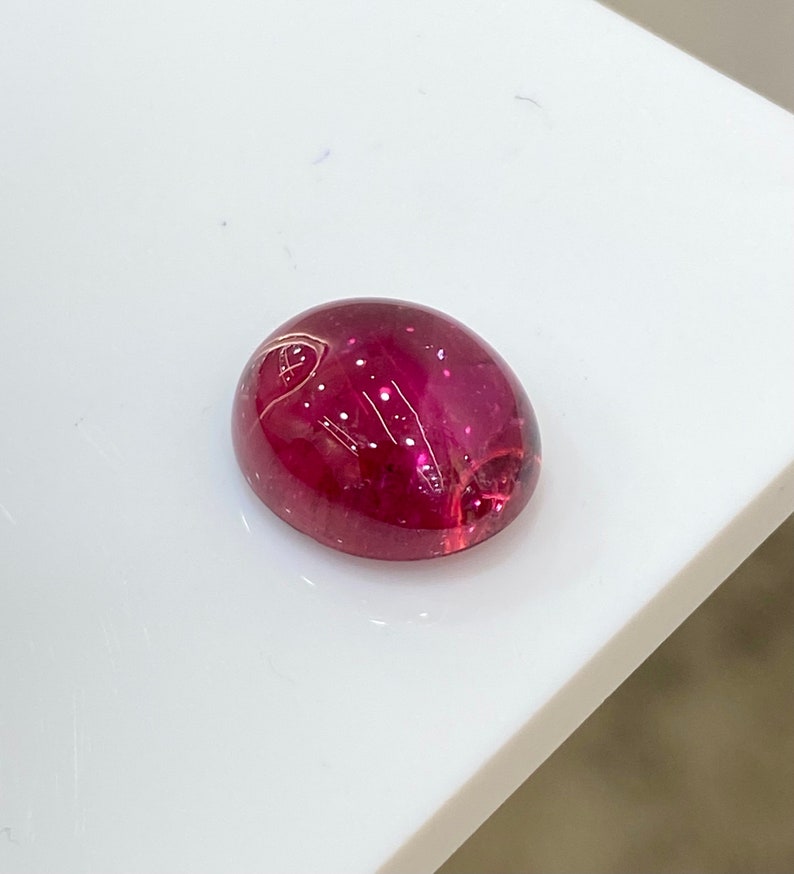 May include: A deep red oval cabochon gemstone with a smooth, polished surface.