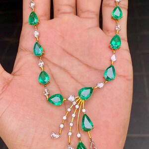 May include: A gold necklace featuring pear-shaped emeralds and small clear gemstones. The emeralds are a vibrant green, and the clear gemstones are set in a delicate pattern. The necklace has a classic and elegant design.