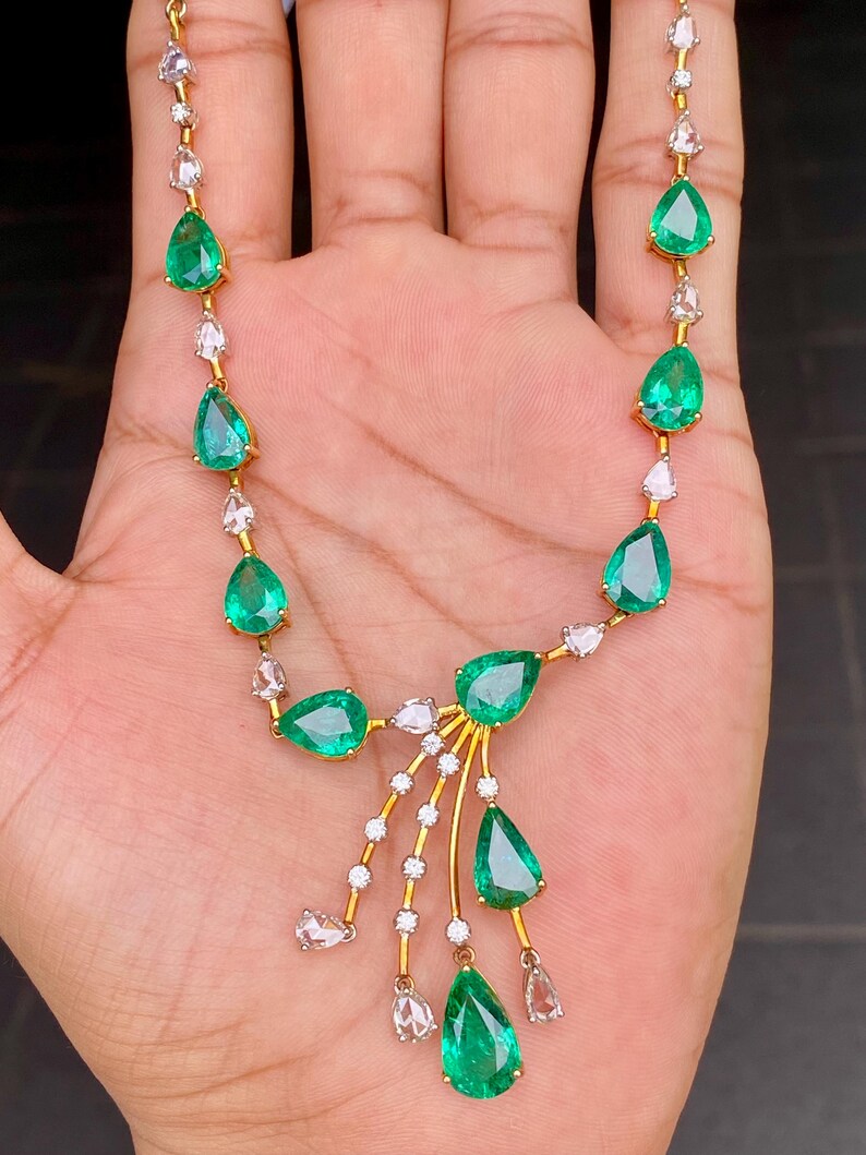 May include: A gold necklace featuring pear-shaped emeralds and small clear gemstones. The emeralds are a vibrant green, and the clear gemstones are set in a delicate pattern. The necklace has a classic and elegant design.