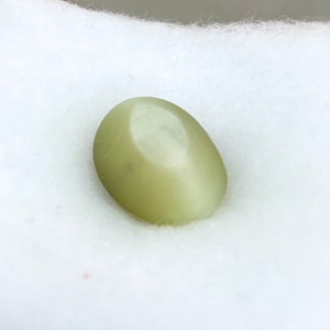 May include: A smooth, oval-shaped green gemstone with a light sheen.