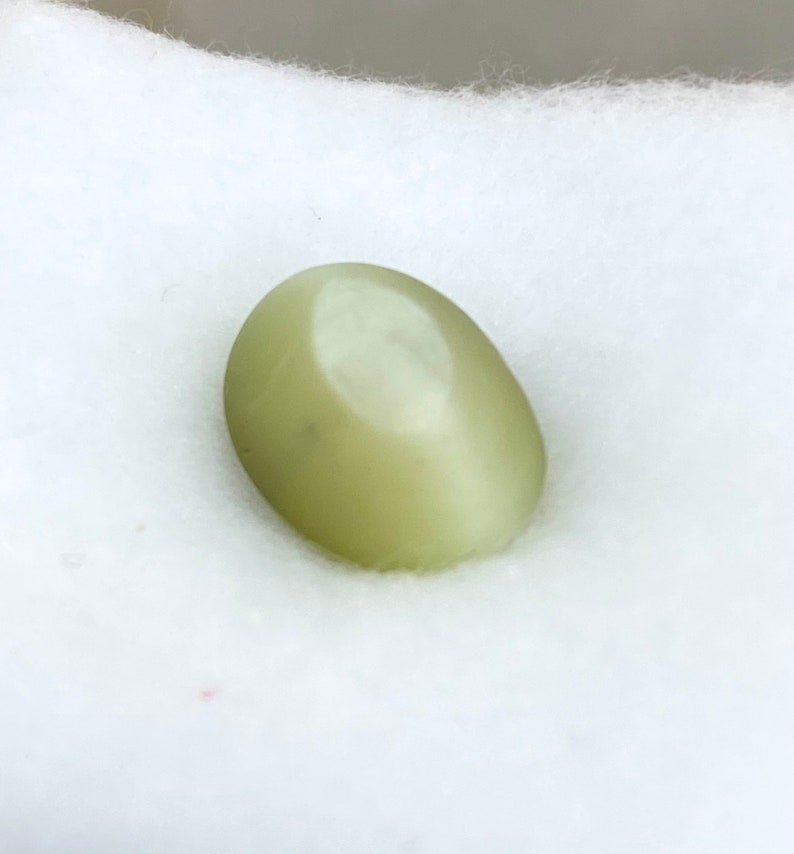 May include: A smooth, oval-shaped green gemstone with a light sheen.