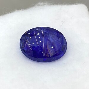 May include: A deep blue oval gemstone with white inclusions. The gemstone is set against a white background.