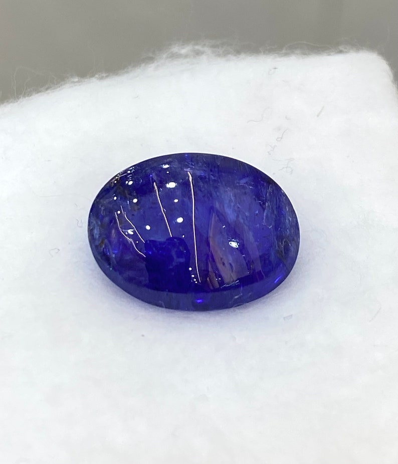 May include: A deep blue oval gemstone with white inclusions. The gemstone is set against a white background.