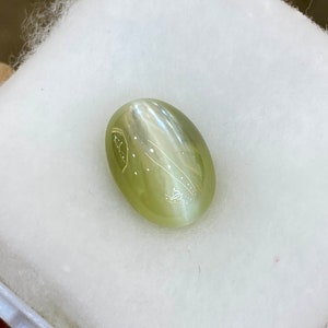 May include: A light green oval-shaped gemstone with a chatoyant effect and white markings.