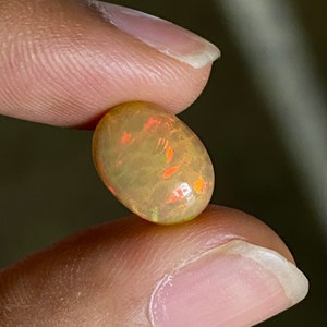 May include: A light green oval opal gemstone with orange and red flashes of color.