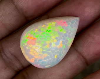 May include: A teardrop-shaped opal cabochon with a white base and iridescent green, orange, and pink flashes.