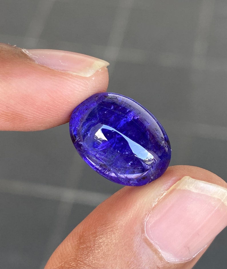 May include: A deep blue oval-shaped gemstone with a smooth, polished surface. The stone has a slight shimmer and a hint of purple.