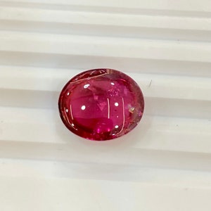May include: A round, pink gemstone with a smooth, polished surface.