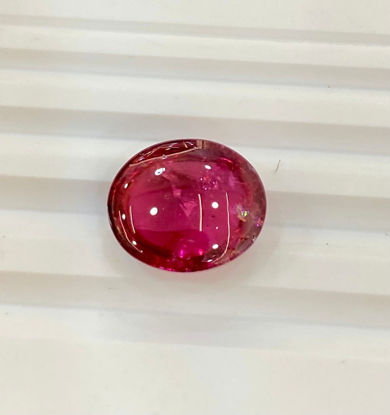 May include: A round, pink gemstone with a smooth, polished surface.