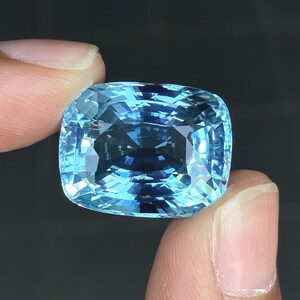 May include: A large, cushion-cut aquamarine gemstone with a light blue color. The gemstone is faceted and has a high degree of brilliance.
