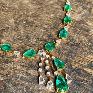 May include: A gold necklace featuring emerald and diamond gemstones. The necklace has a delicate design with pear-shaped emeralds and round diamonds. The gemstones are set in gold, creating a luxurious and elegant look.