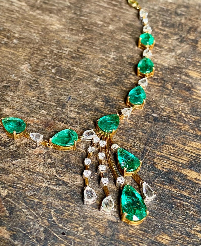 May include: A gold necklace featuring emerald and diamond gemstones. The necklace has a delicate design with pear-shaped emeralds and round diamonds. The gemstones are set in gold, creating a luxurious and elegant look.