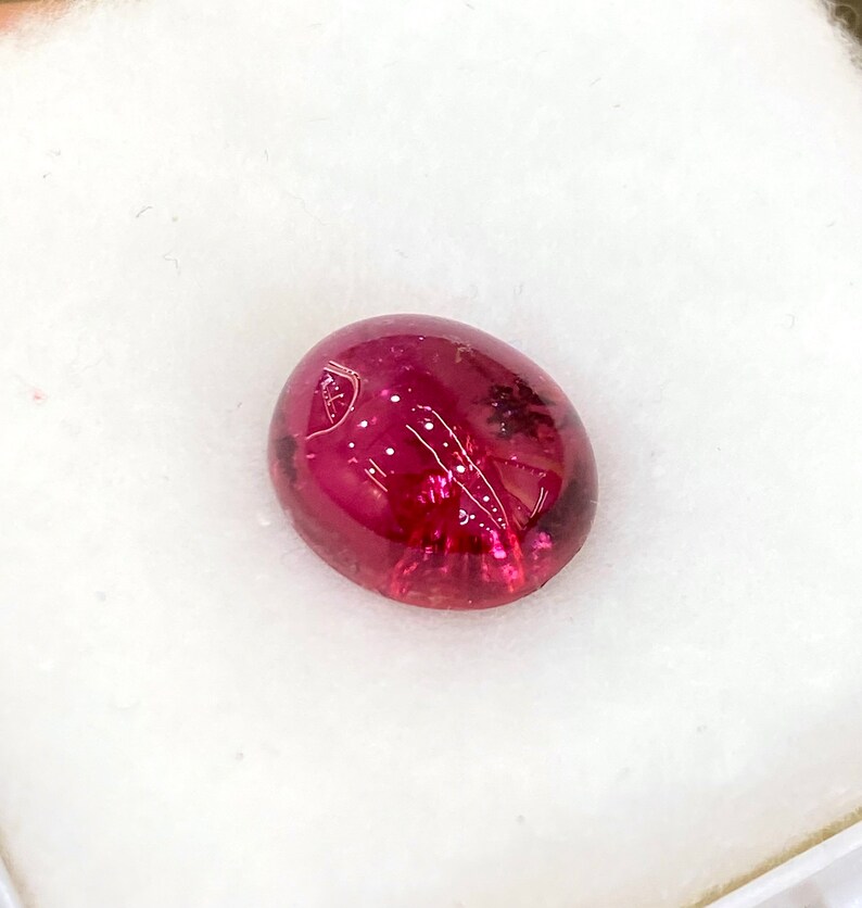 May include: A deep red oval cabochon gemstone with a smooth, polished surface.