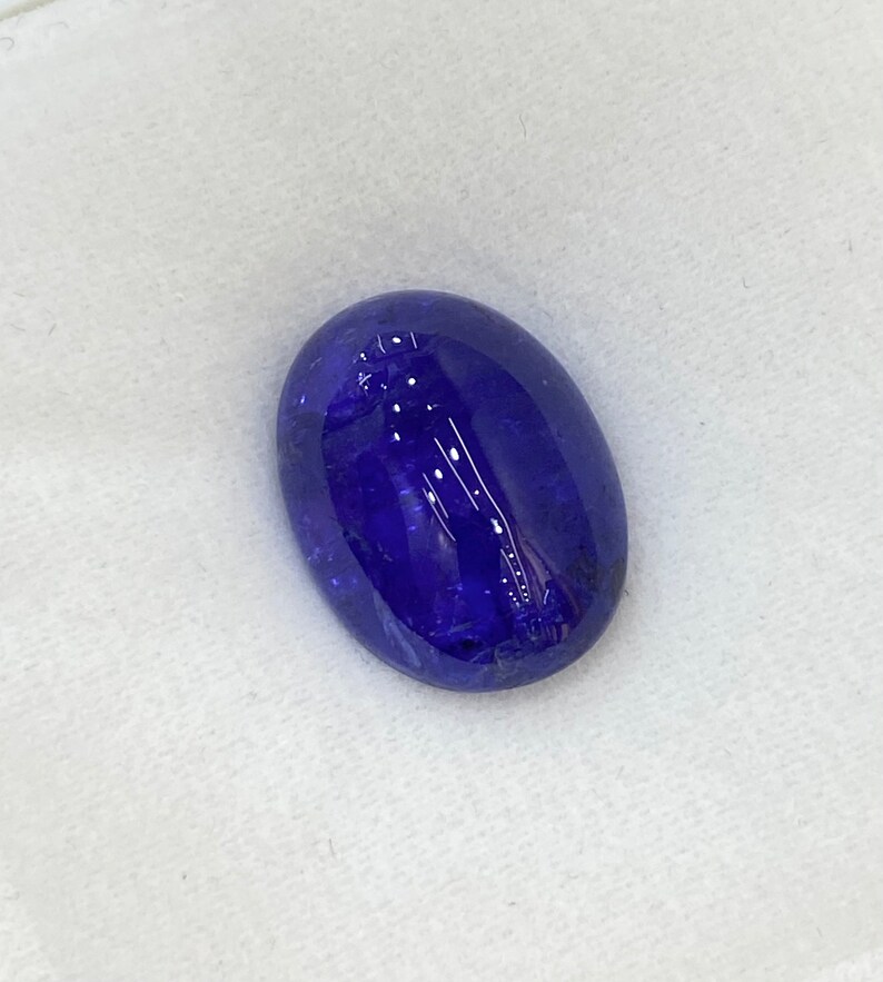 May include: A deep blue oval-shaped gemstone with a smooth, polished surface.