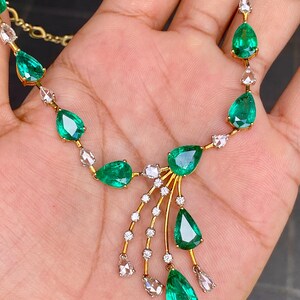 May include: A gold necklace featuring pear-shaped emeralds and small, clear gemstones. The emeralds are a vibrant green, and the necklace has a delicate, elegant design. The gemstones are set in a gold chain.