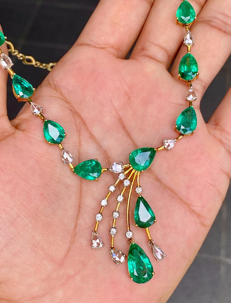 May include: A gold necklace featuring pear-shaped emeralds and small, clear gemstones. The emeralds are a vibrant green, and the necklace has a delicate, elegant design. The gemstones are set in a gold chain.