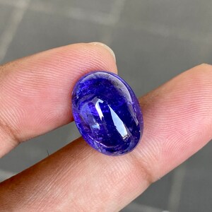 May include: A deep blue oval-shaped gemstone with a smooth, polished surface. The gemstone has a slight shimmer and is set in a clear, transparent setting.